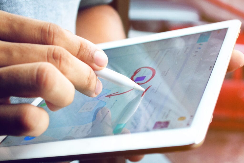 A hand holding a pen to draw on a tablet to emphasize certain information in data analytics.