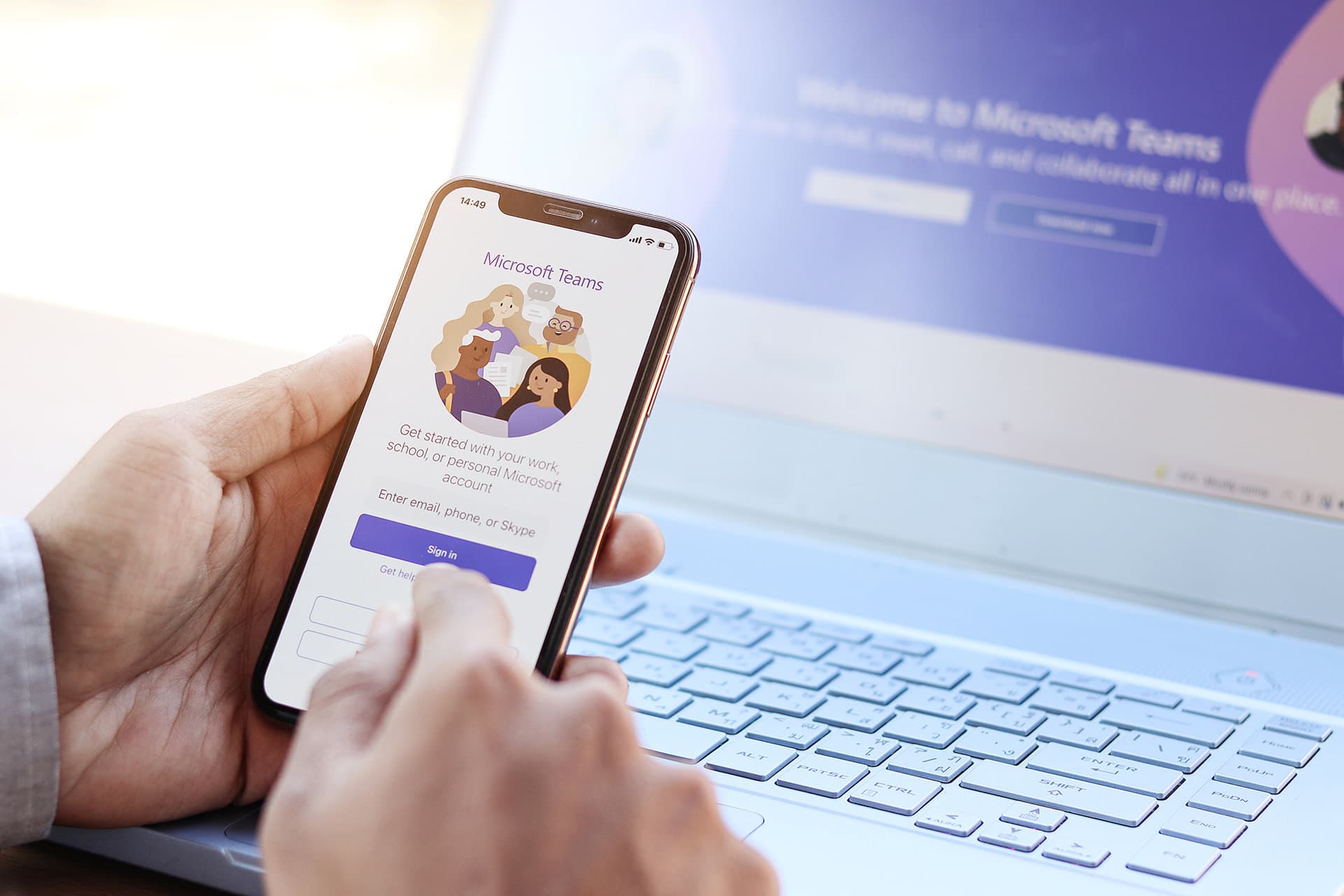 A person holding a phone in front of a laptop to show unified communications across multiple devices through Microsoft Teams.
