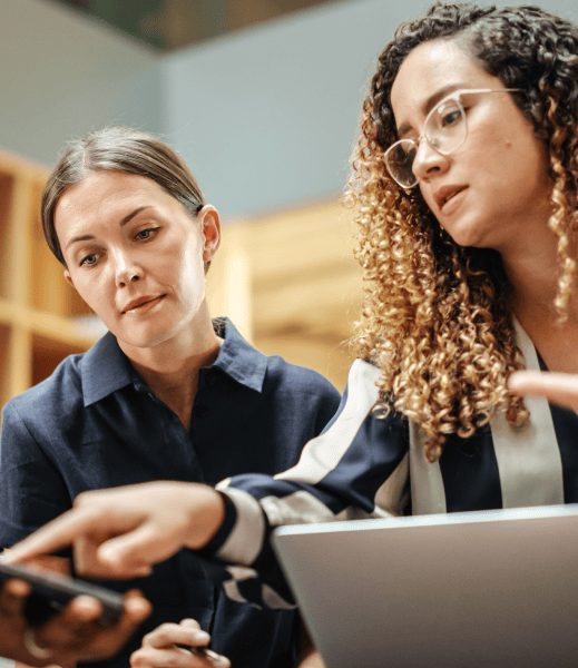 Two women looking at a phone and analysing what they see.