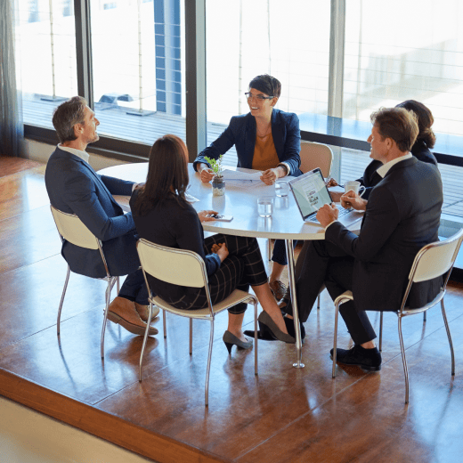 Five co-workers sitting at a round table in a meeting room.