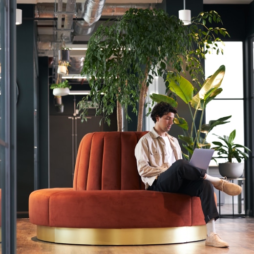 Man sitting on a comfortable bench working on his laptop.