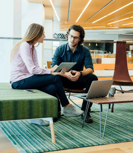 Two people sitting in an office building looking at a tablet.