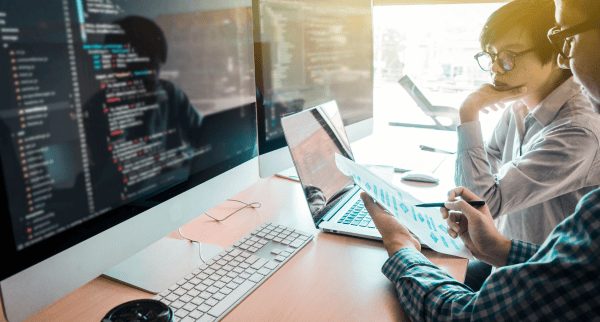 Two developers looking at big screens with lines of code.