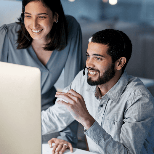 Two coworkers wearing headsets look at a big desktop screen in the office