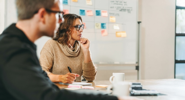 Two-coworkers in a meeting room. They’re looking at something that is not in the picture.