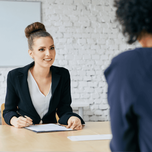 Two women sitting in a meeting room table discussing a paper.