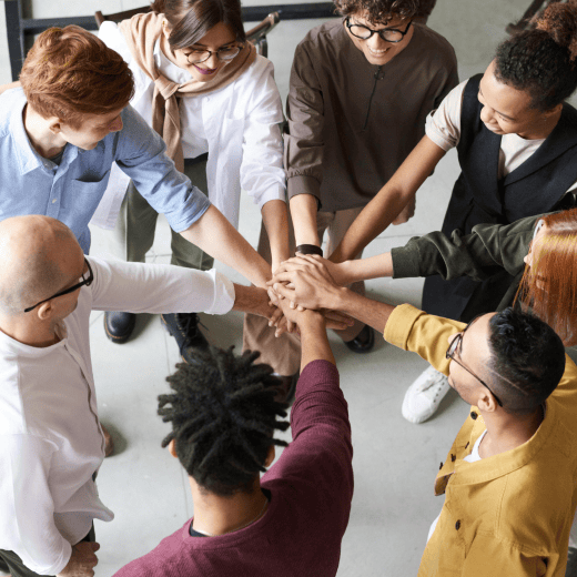 A team of coworkers standing in a circle with stretched out arms to reach each others hands and symbolize connection.