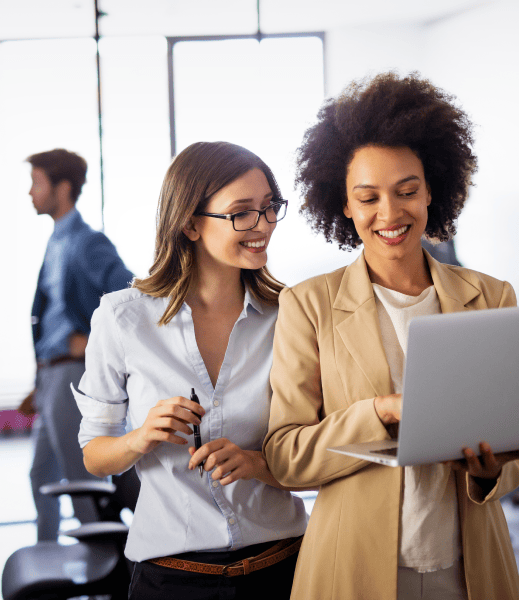 Two women stood in an office are looking at a laptop screen