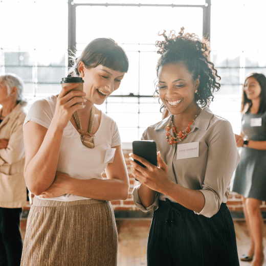 Two women in an office environment looking at a phone with excitement