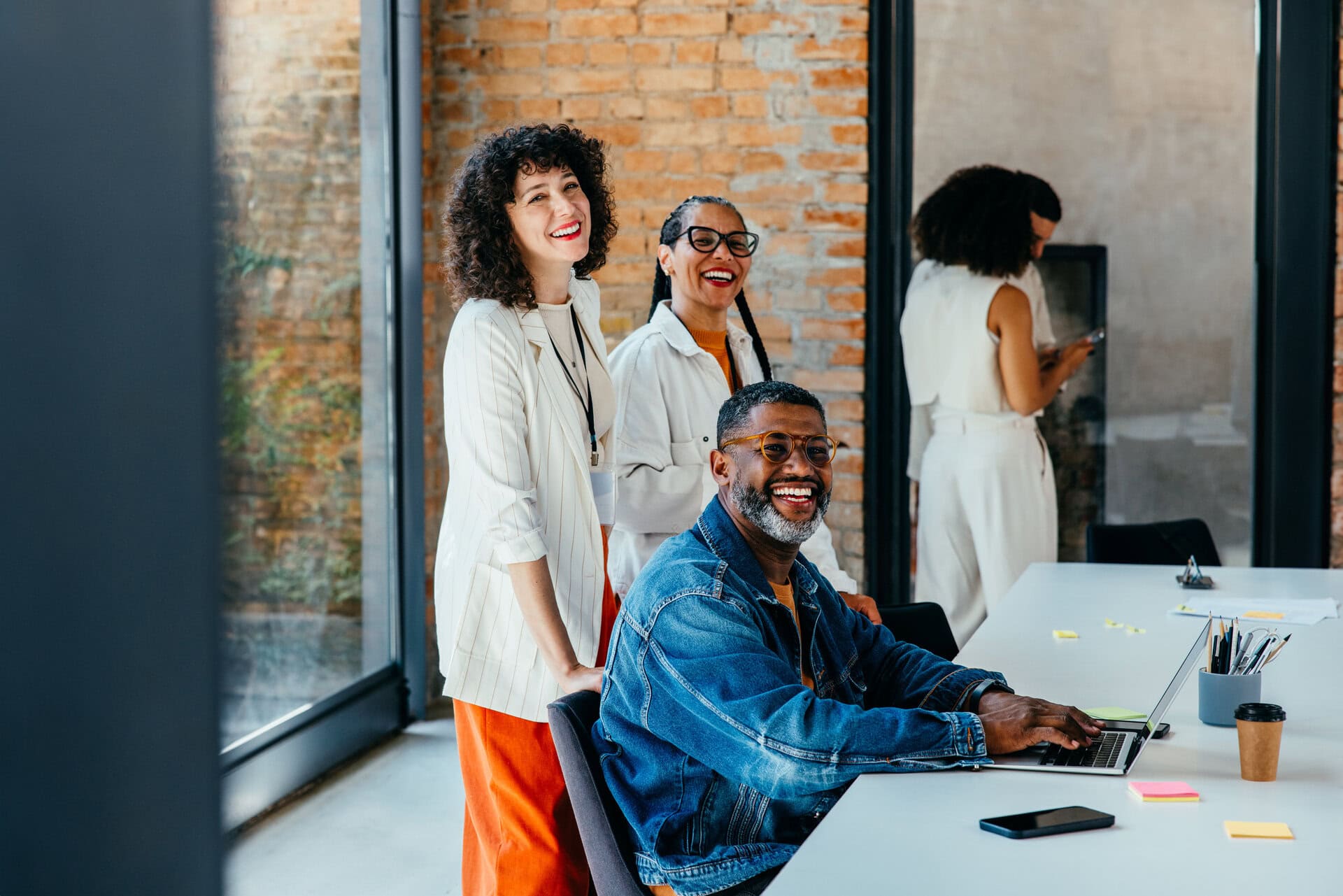 A diverse team joyfully collaborates in a trendy office setting with ample natural light, fostering creativity and teamwork.